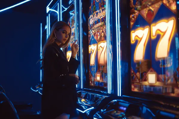 SPORTYBEF Slots — Thousands of thrilling machines await A woman smiling by bright slot machines showing lucky symbols, showcasing the exciting slot offerings at SPORTYBEF.